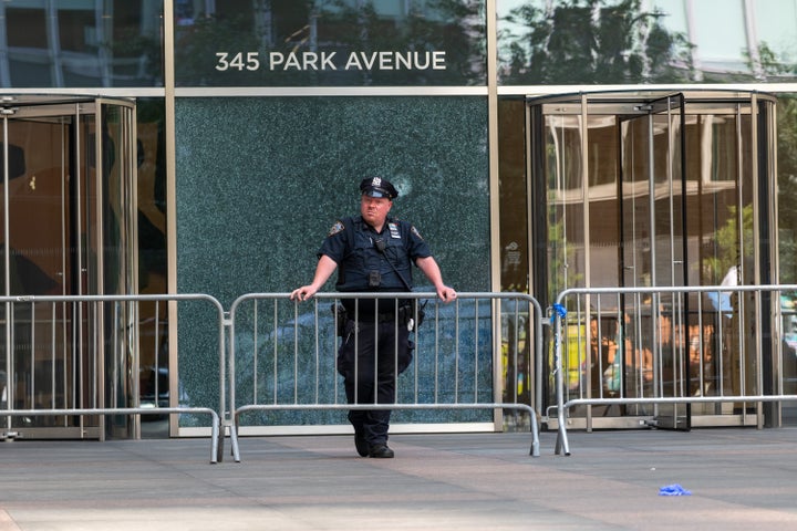 A New York Police Department (NYPD) officer stands in front of a bullet-shattered window at 345 Park Avenue building on Park Avenue after a gunman killed four people before turning the gun on himself on Monday evening on July 29, 2025, in New York City. The suspect, identified as Shane Tamura, 27, shot and killed a police officer and three civilians, the New York Police Department has said. (Photo by Spencer Platt/Getty Images)